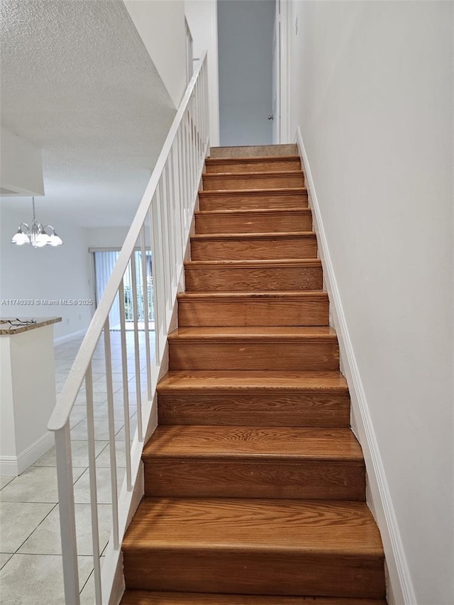 stairs featuring tile patterned flooring, an inviting chandelier, and a textured ceiling