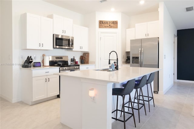 kitchen with light countertops, appliances with stainless steel finishes, a center island with sink, and white cabinetry