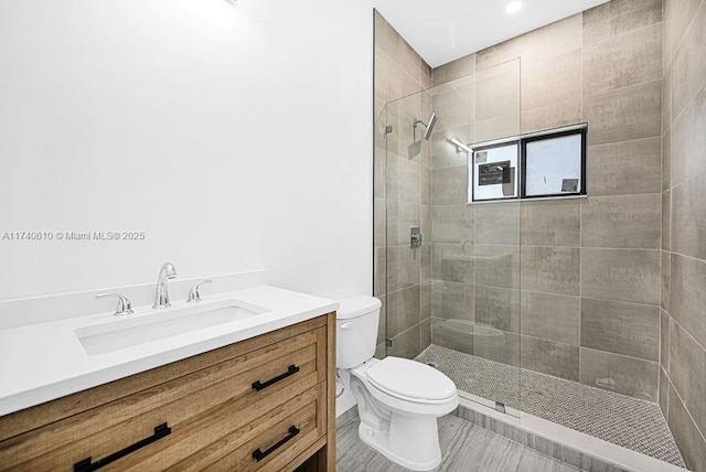 bathroom with tiled shower, vanity, and toilet