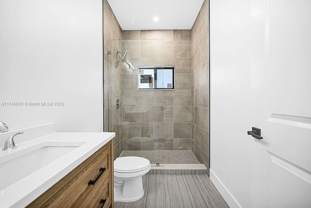 bathroom featuring a tile shower, vanity, and toilet