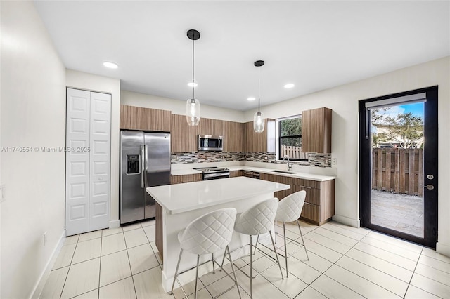 kitchen with light tile patterned floors, hanging light fixtures, stainless steel appliances, tasteful backsplash, and a kitchen island