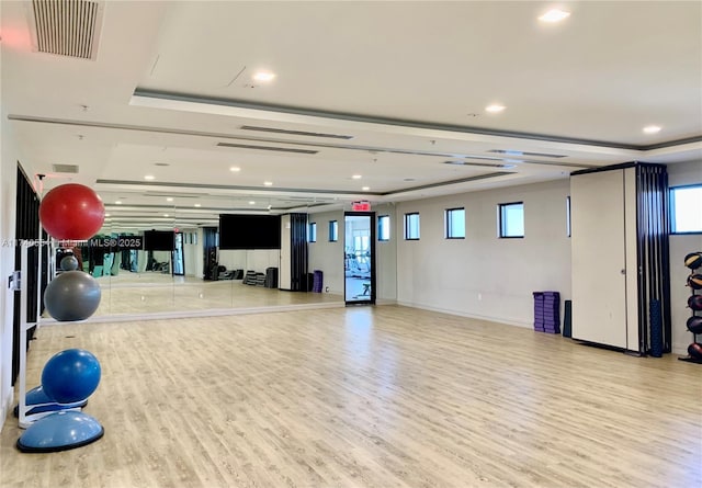 gym with a wealth of natural light, light wood-type flooring, and a tray ceiling