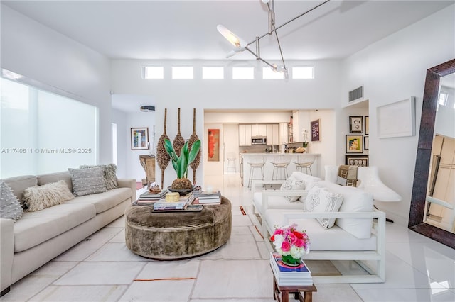 living room featuring light tile patterned floors, visible vents, a wealth of natural light, and a towering ceiling