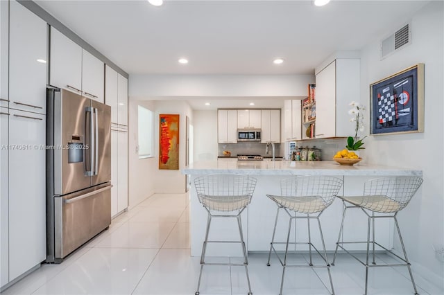 kitchen featuring appliances with stainless steel finishes, a sink, a breakfast bar area, a peninsula, and visible vents
