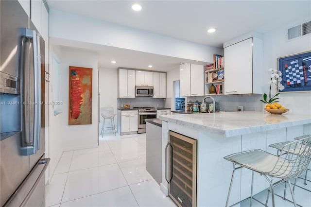 kitchen with appliances with stainless steel finishes, beverage cooler, a kitchen bar, backsplash, and visible vents