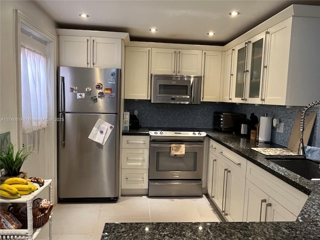 kitchen featuring sink, light tile patterned floors, appliances with stainless steel finishes, dark stone countertops, and decorative backsplash