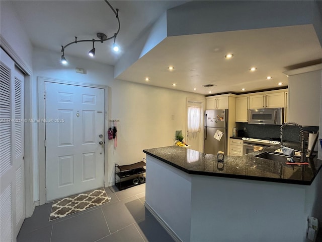 kitchen featuring appliances with stainless steel finishes, white cabinetry, sink, light tile patterned floors, and kitchen peninsula