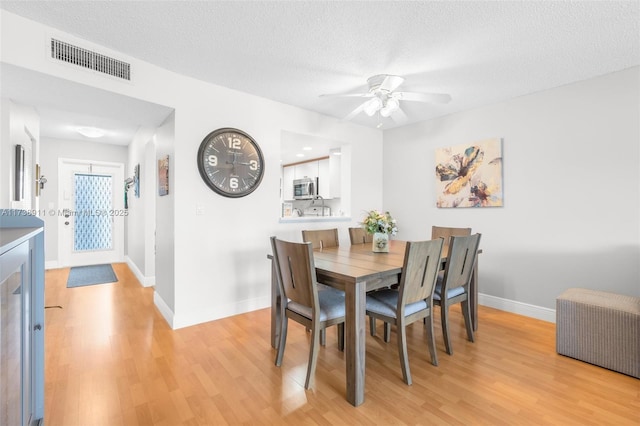 dining space with ceiling fan, a textured ceiling, and light hardwood / wood-style floors