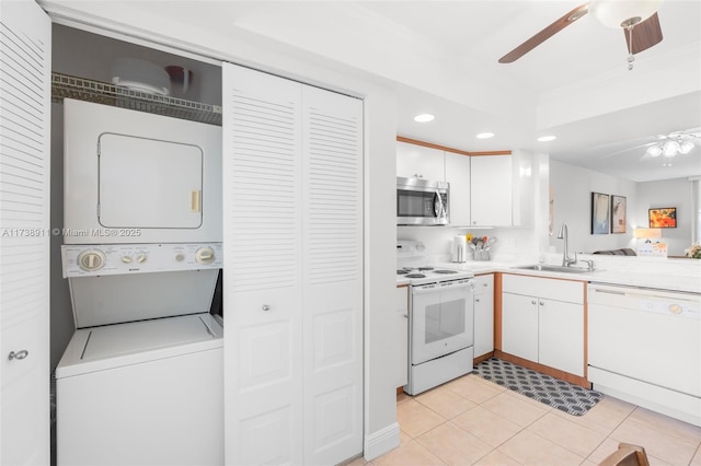 kitchen featuring sink, white appliances, ceiling fan, stacked washing maching and dryer, and white cabinets