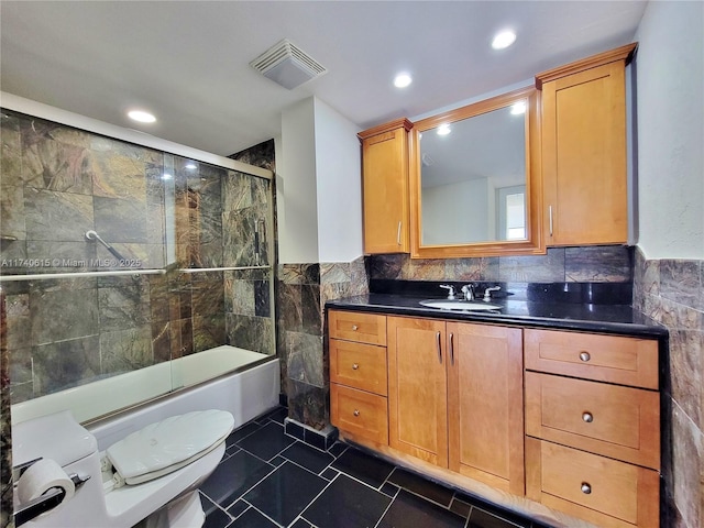 full bathroom with shower / bath combination with glass door, vanity, toilet, and tile walls