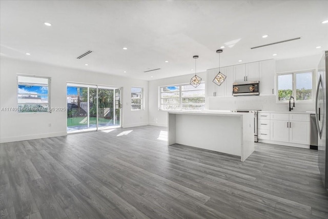 kitchen with appliances with stainless steel finishes, a center island, white cabinets, dark hardwood / wood-style flooring, and decorative light fixtures