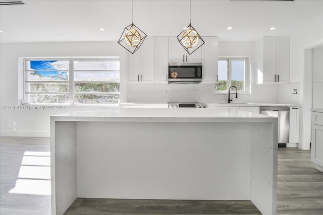 kitchen featuring a kitchen island, appliances with stainless steel finishes, white cabinets, hanging light fixtures, and light stone counters