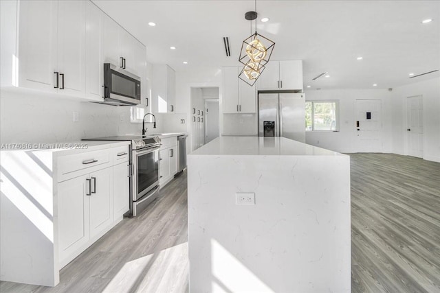 kitchen with white cabinets, hanging light fixtures, a center island, stainless steel appliances, and light hardwood / wood-style flooring