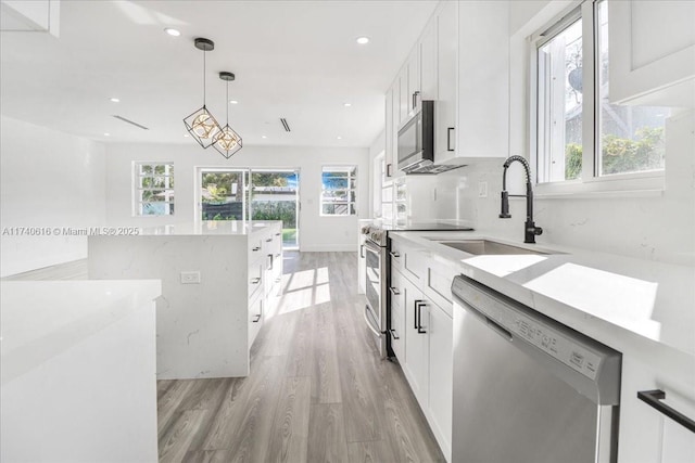 kitchen featuring sink, appliances with stainless steel finishes, white cabinetry, hanging light fixtures, and a healthy amount of sunlight