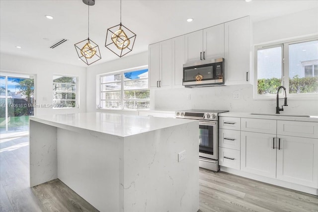 kitchen featuring pendant lighting, sink, appliances with stainless steel finishes, white cabinetry, and light wood-type flooring