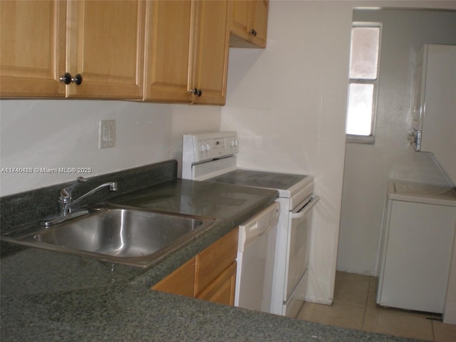 kitchen with white appliances, light tile patterned floors, washer / dryer, dark countertops, and a sink