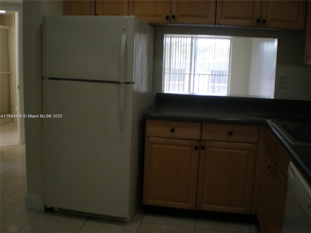 kitchen featuring dark countertops, white appliances, light tile patterned flooring, and a sink