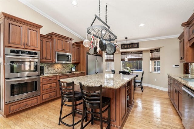 kitchen with appliances with stainless steel finishes, hanging light fixtures, ornamental molding, a kitchen island, and decorative backsplash