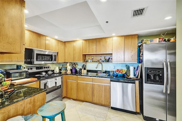 kitchen with visible vents, a sink, dark stone counters, appliances with stainless steel finishes, and a raised ceiling