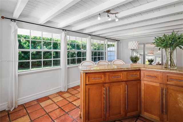 kitchen featuring light stone counters, track lighting, a healthy amount of sunlight, and beam ceiling