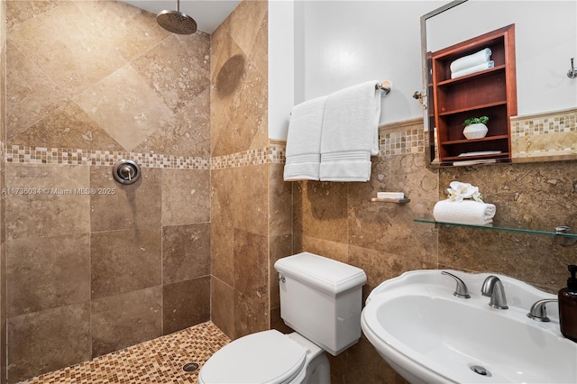 bathroom with sink, a tile shower, tile walls, and toilet