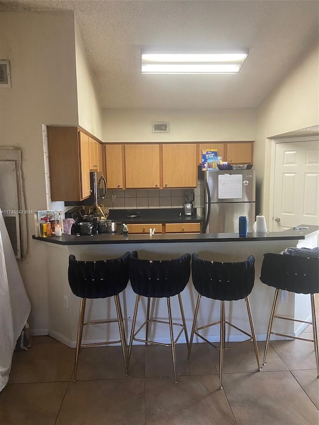 kitchen with a kitchen bar, stainless steel fridge, kitchen peninsula, and backsplash