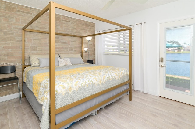 bedroom with hardwood / wood-style flooring, brick wall, a water view, and ceiling fan