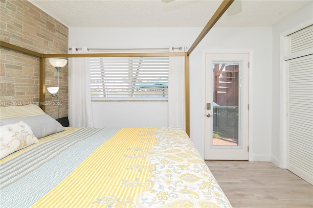 bedroom with access to exterior, brick wall, a textured ceiling, and light wood-type flooring