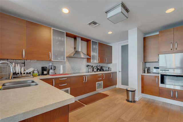 kitchen featuring sink, backsplash, fridge, light wood-type flooring, and wall chimney exhaust hood