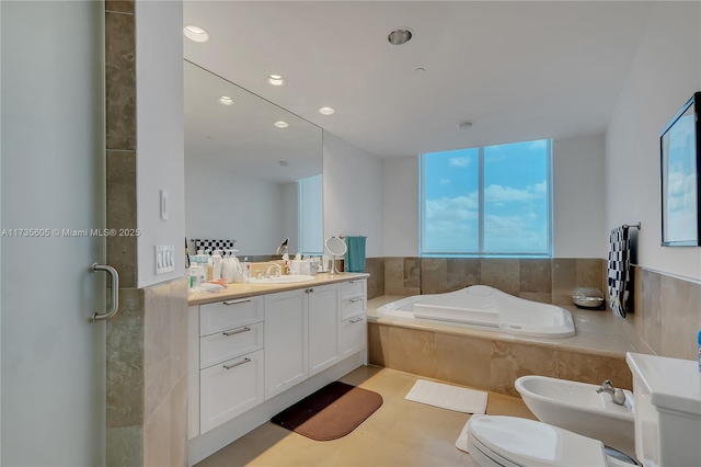 bathroom with tiled tub, a bidet, vanity, and toilet