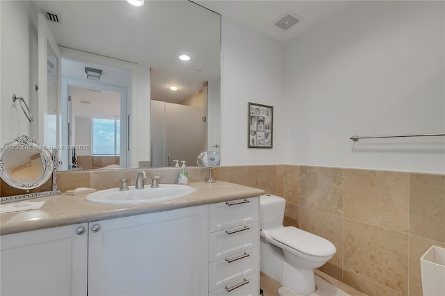 bathroom featuring walk in shower, vanity, toilet, and tile walls