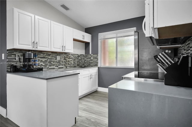 kitchen featuring lofted ceiling, sink, white cabinets, decorative backsplash, and light wood-type flooring