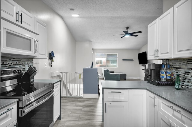 kitchen with stainless steel electric stove, white cabinets, decorative backsplash, ceiling fan, and kitchen peninsula