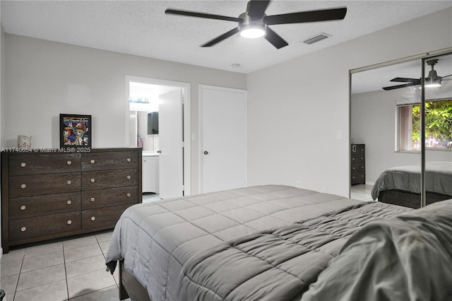 tiled bedroom with ceiling fan, a closet, ensuite bathroom, and a textured ceiling