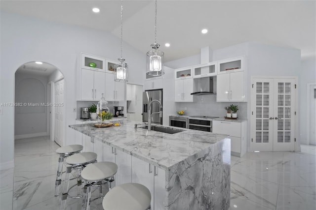 kitchen with a spacious island, wall chimney exhaust hood, sink, decorative light fixtures, and white cabinets