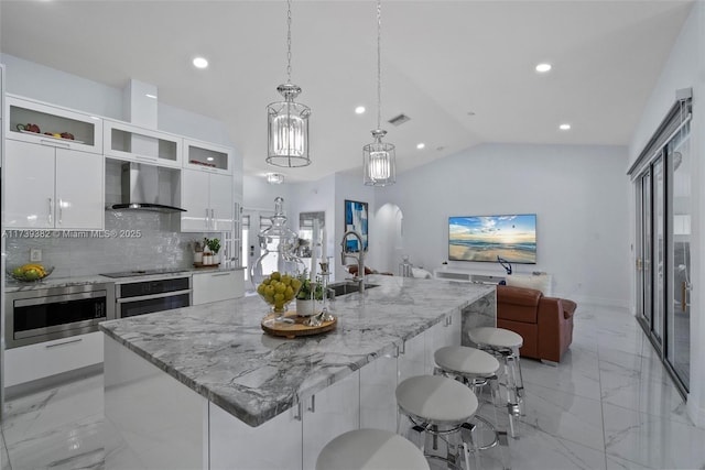 kitchen featuring sink, white cabinetry, wall chimney exhaust hood, an island with sink, and stainless steel oven