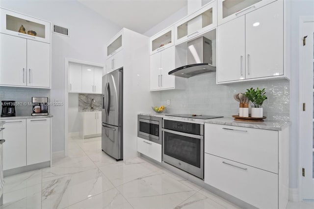 kitchen with tasteful backsplash, white cabinetry, stainless steel appliances, light stone countertops, and wall chimney exhaust hood