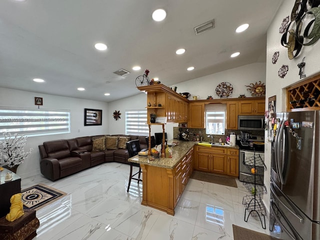 kitchen with a breakfast bar, stainless steel appliances, light stone countertops, vaulted ceiling, and kitchen peninsula