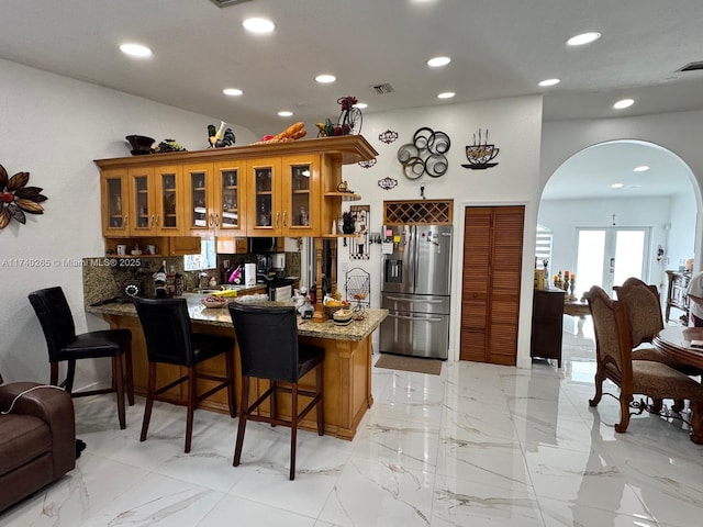 kitchen with stainless steel fridge, kitchen peninsula, vaulted ceiling, and light stone countertops