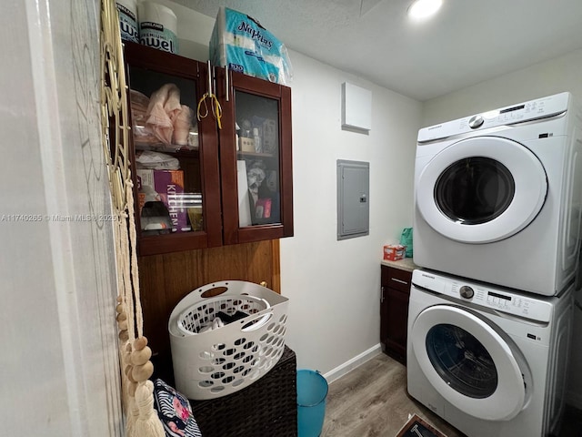 clothes washing area with stacked washer and dryer, electric panel, and light hardwood / wood-style floors