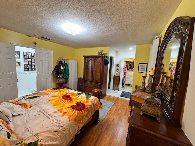 bedroom featuring a closet, a walk in closet, a textured ceiling, and light hardwood / wood-style flooring