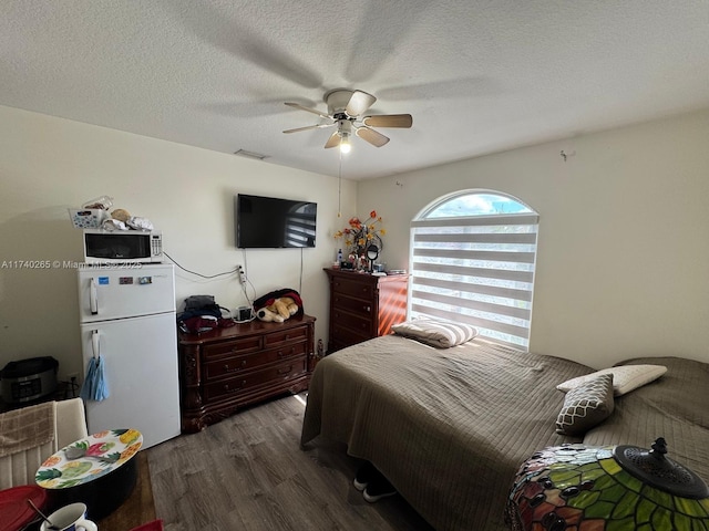 bedroom featuring white refrigerator, ceiling fan, dark wood-type flooring, and a textured ceiling