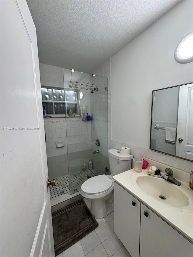 bathroom featuring a shower with shower door, tile patterned flooring, vanity, toilet, and a textured ceiling