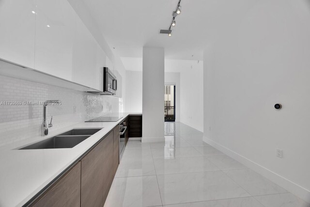 kitchen with appliances with stainless steel finishes, white cabinetry, rail lighting, sink, and backsplash
