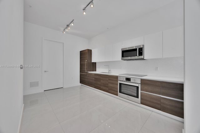 kitchen featuring appliances with stainless steel finishes, white cabinetry, sink, backsplash, and light tile patterned floors