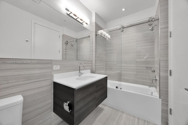 full bathroom with bath / shower combo with glass door, tile walls, vanity, and toilet