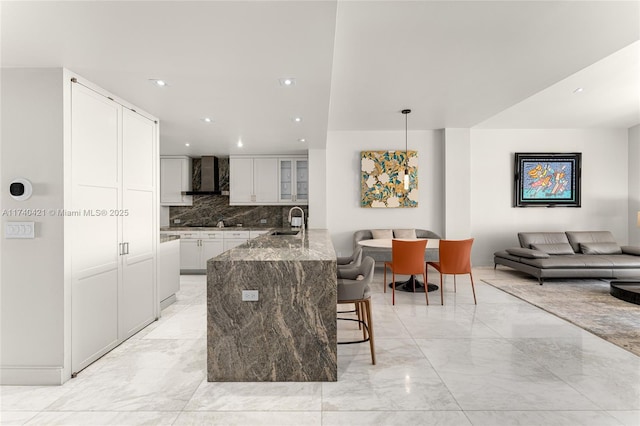 kitchen featuring decorative light fixtures, sink, white cabinets, light stone countertops, and wall chimney exhaust hood