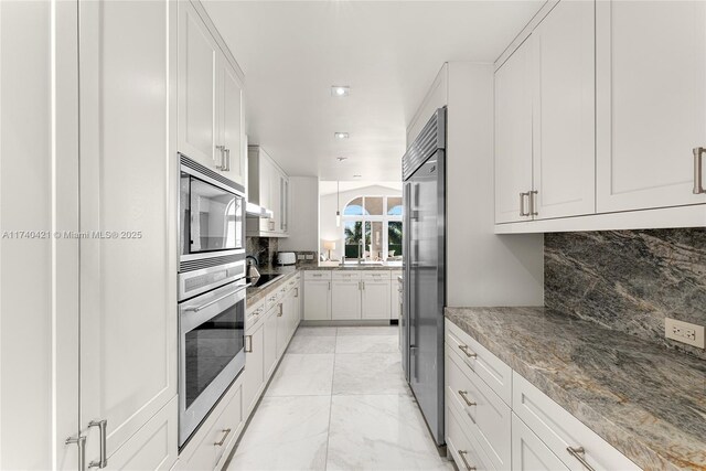 kitchen featuring white cabinetry, appliances with stainless steel finishes, light stone countertops, and tasteful backsplash