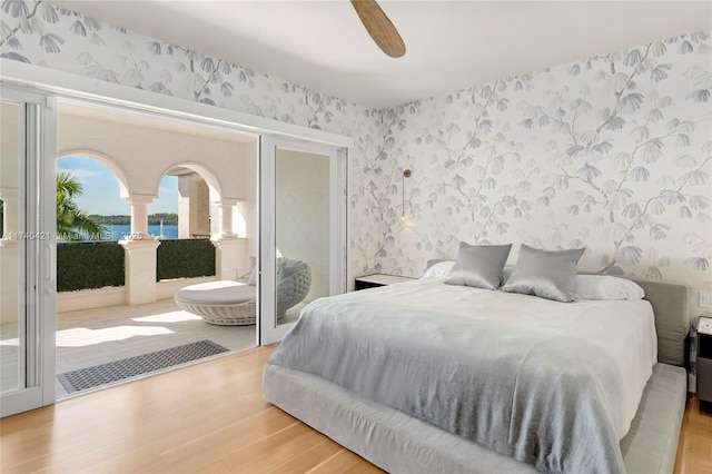 bedroom featuring a water view, ceiling fan, access to exterior, and light wood-type flooring