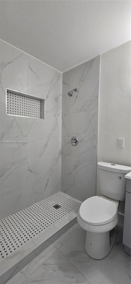 bathroom featuring vanity, tiled shower, a textured ceiling, and toilet